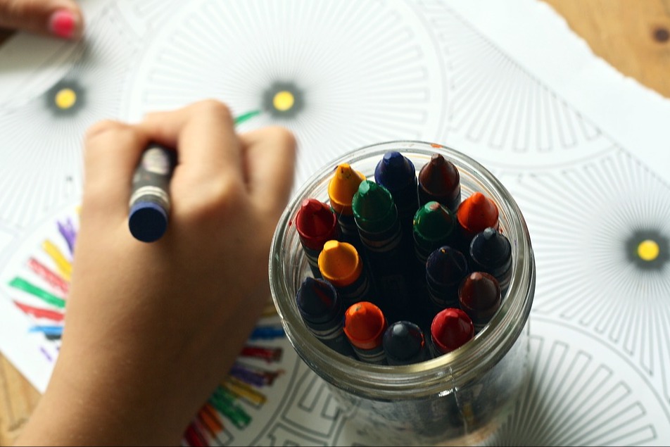 A child's hand next to a jar of crayons, coloring a picture