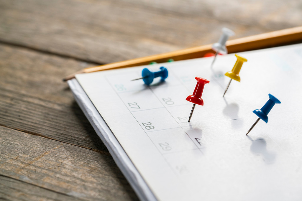 Pins in a calendar sitting on a desk next to a pencil
