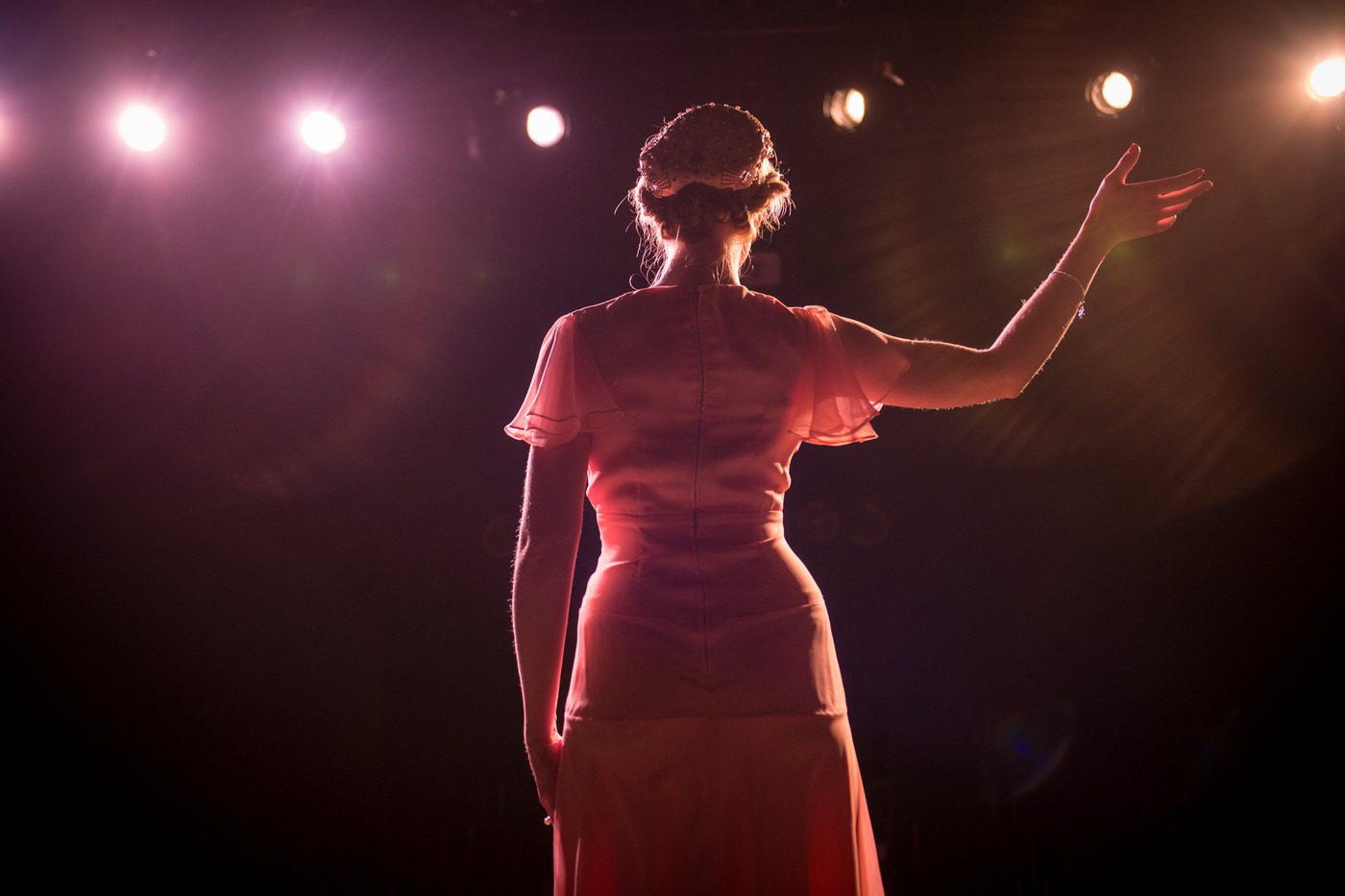 A woman in spotlights raising her right hand to the air, as if standing on a stage