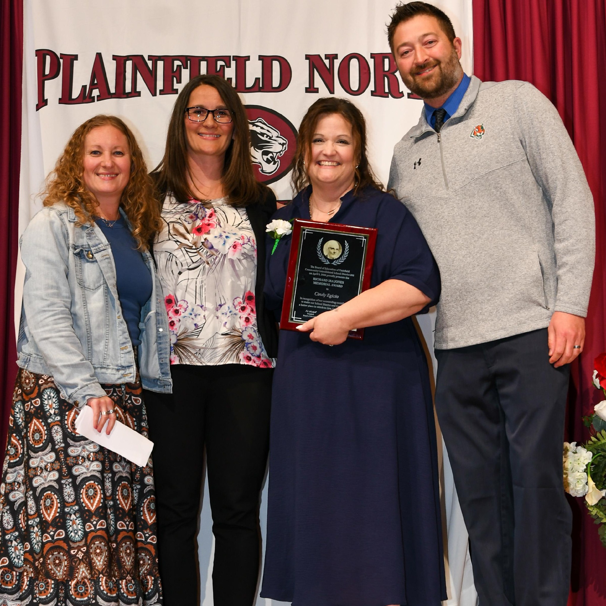 four adults stand in front of Plainfield North banner. One woman holds award plaque