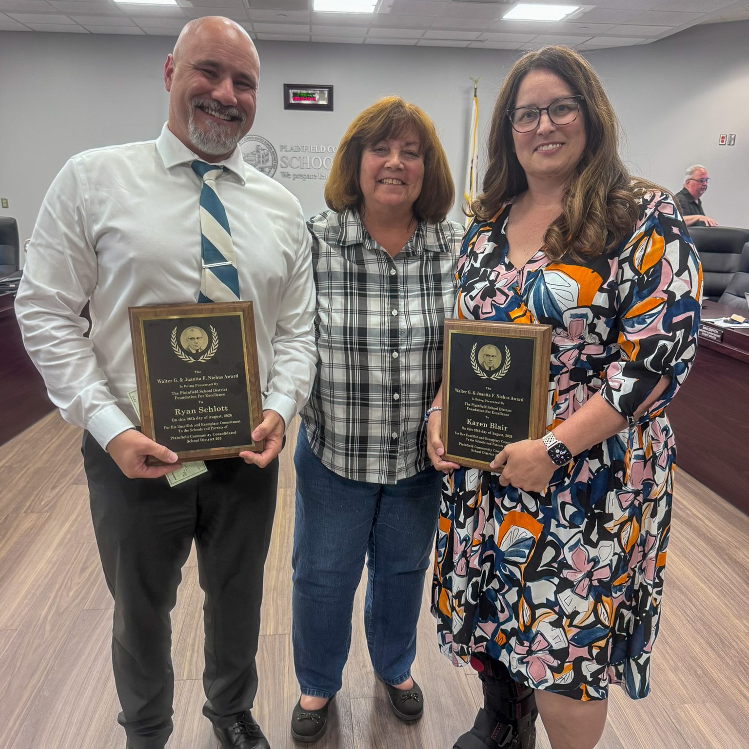 man and woman hold award plaques. Woman who gave them plaques stand in middle