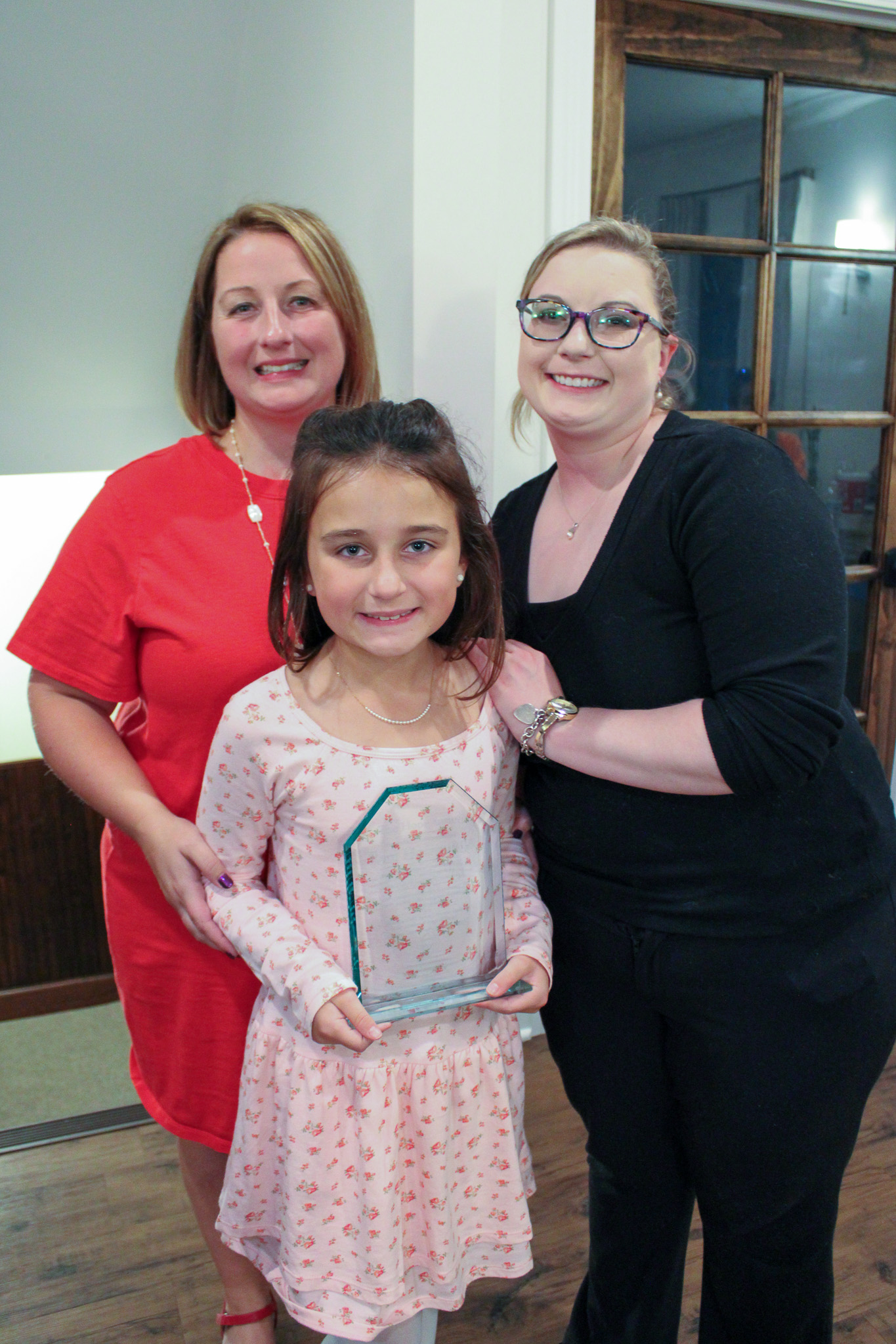 two women and girl stand together. Girl holding clear award