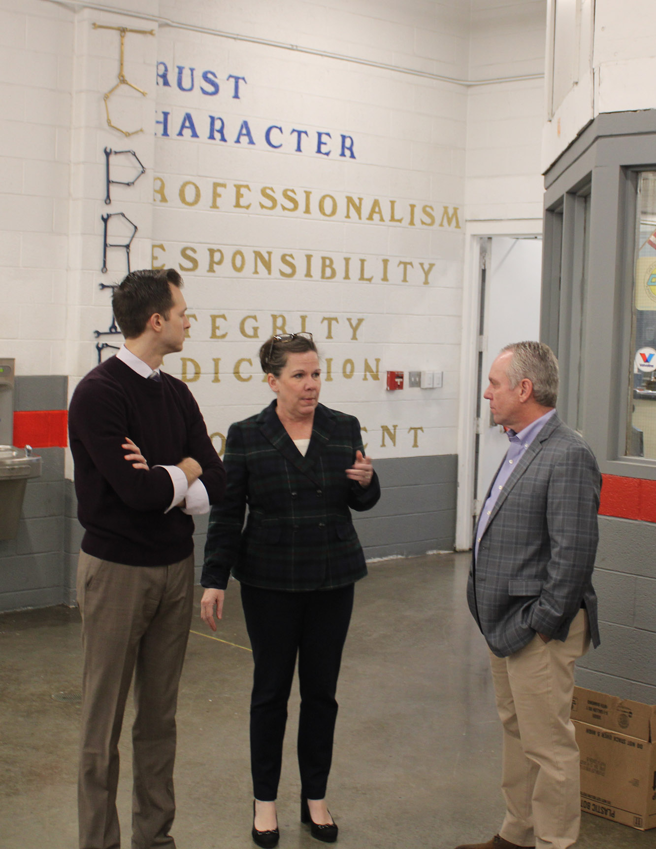 Three people in suits stand in front of acronym mural