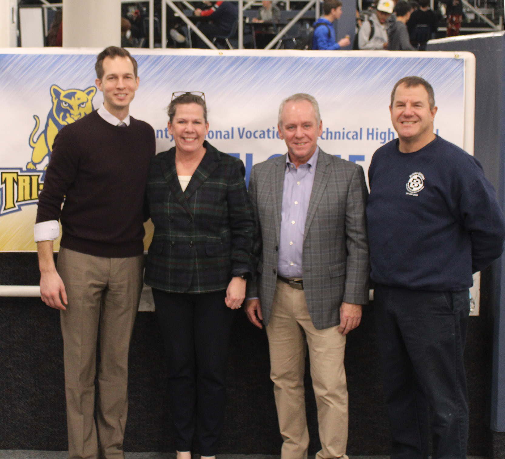 4 people in suits standing in front of school logo