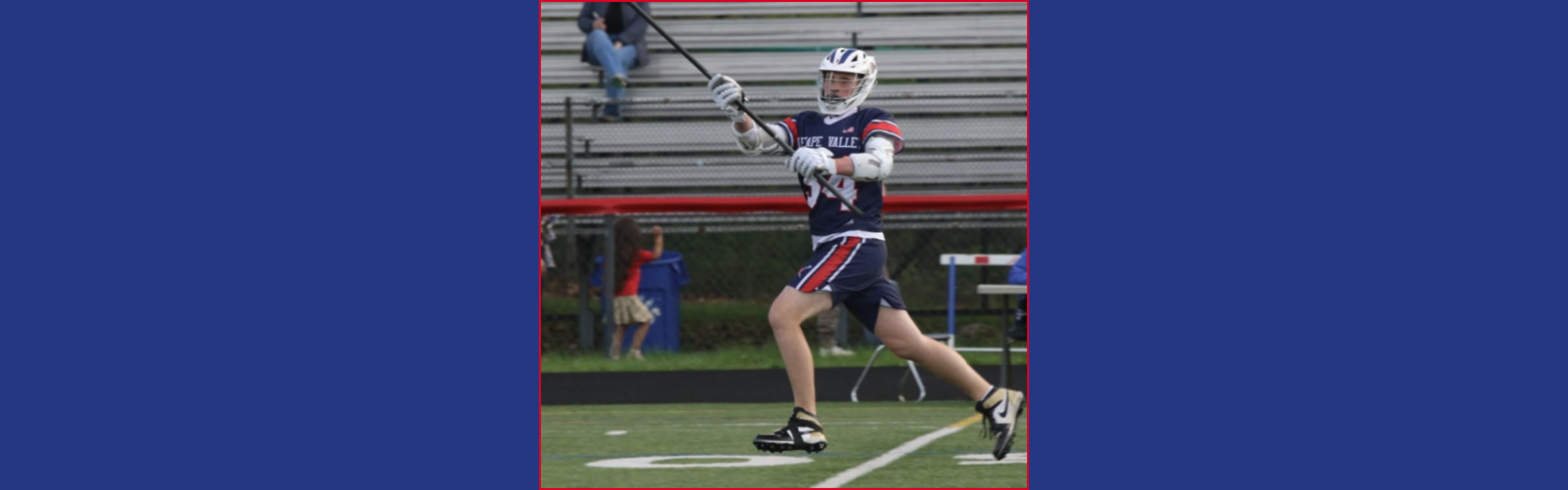 Jaxson Goss runs across the lacrosse field in a Lenape Valley navy, red, and white uniform and helmet, holding his lacrosse stick.
