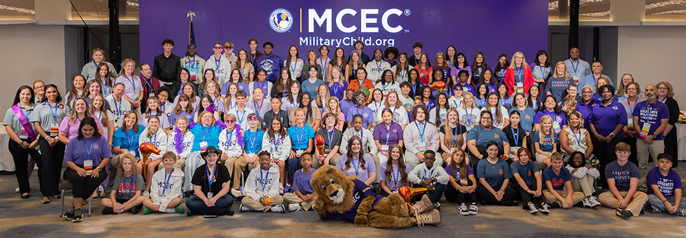 MCEC students seating and standing for a group picture in front of a purple banner with the letters MCEC