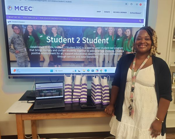 ASFL Mrs. Williams standing next to purple and white striped gift bags in front of a smartboard indicating student 2 student
