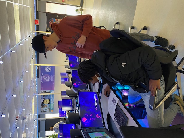 student standing in front of a computer with another student sitting