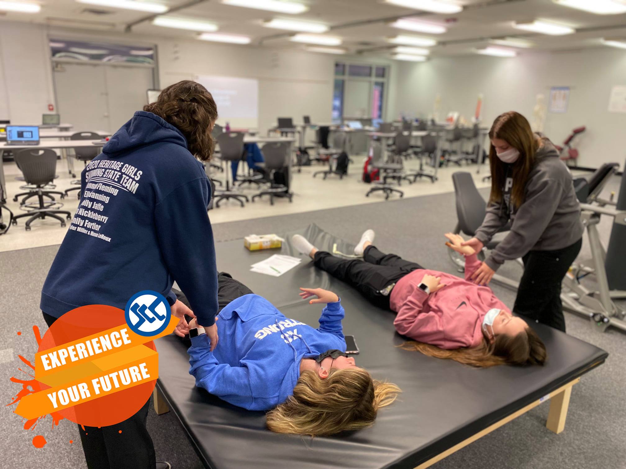 students using technical skills in physical therapy with other students laying on beds