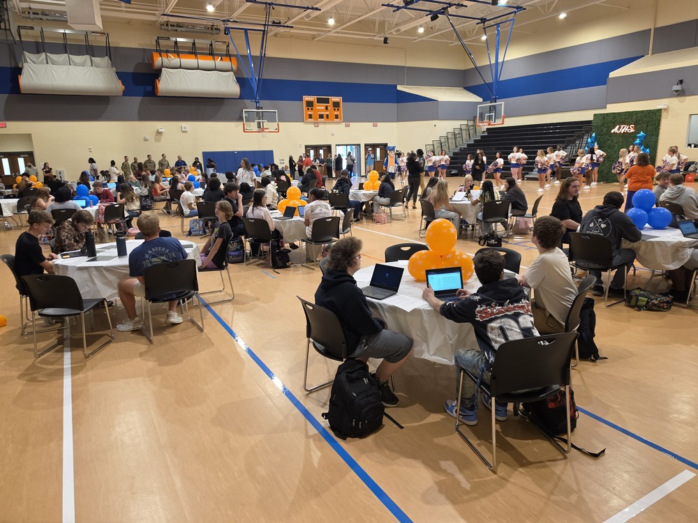 Many people at tables in a gym, with some wearing backpacks. A blue line marks the floor.