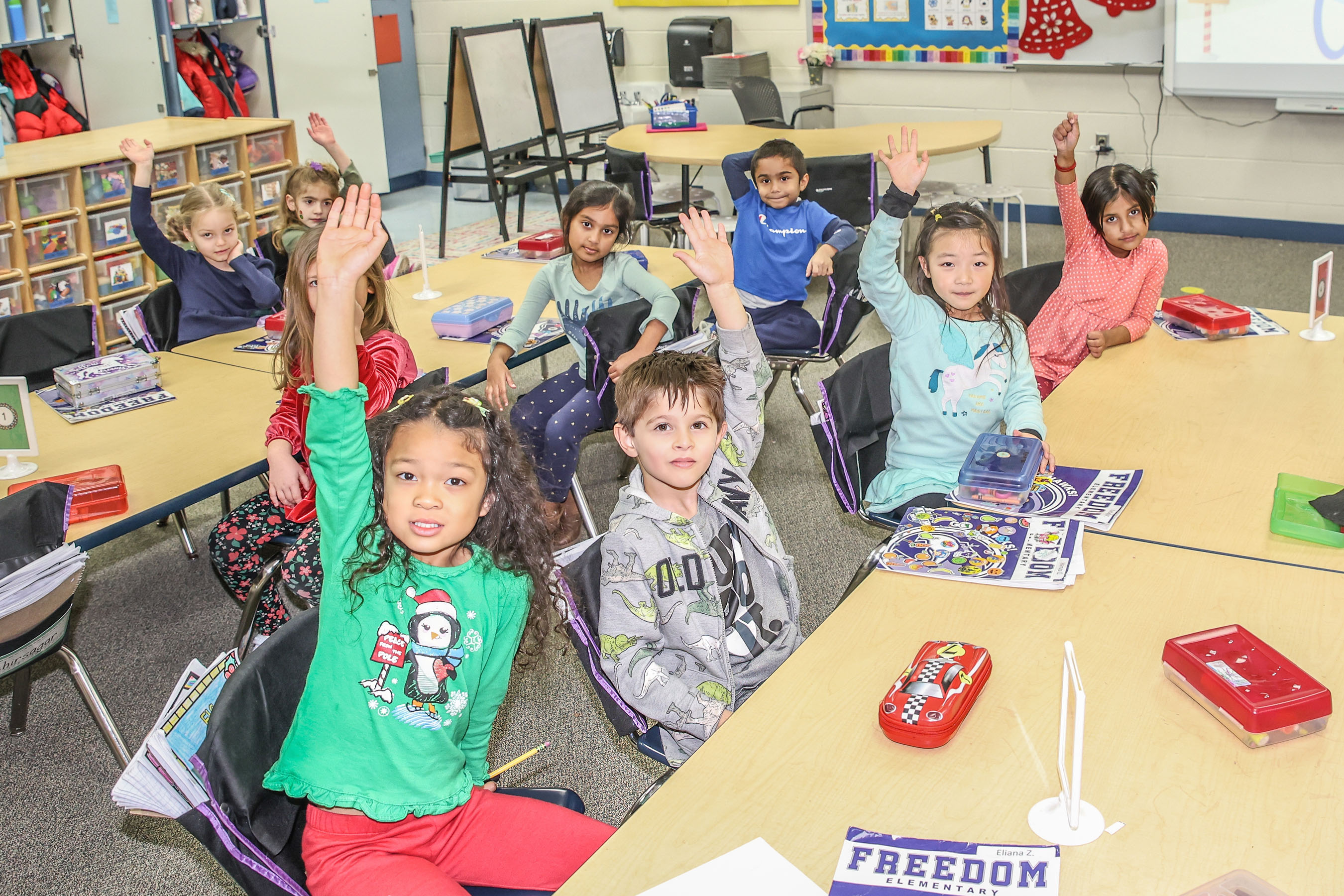 students sitting at table with hands raised