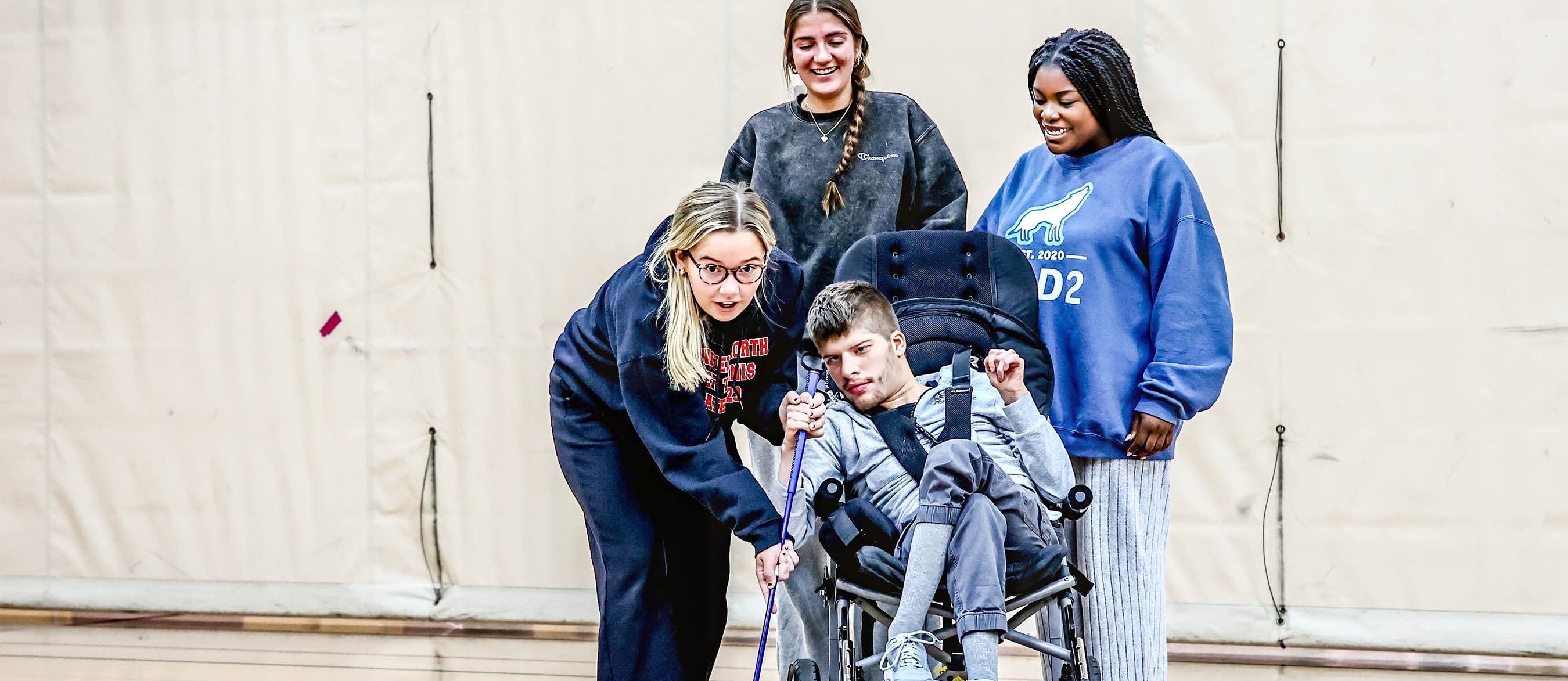 three student guide student in wheelchair in adaptive golf