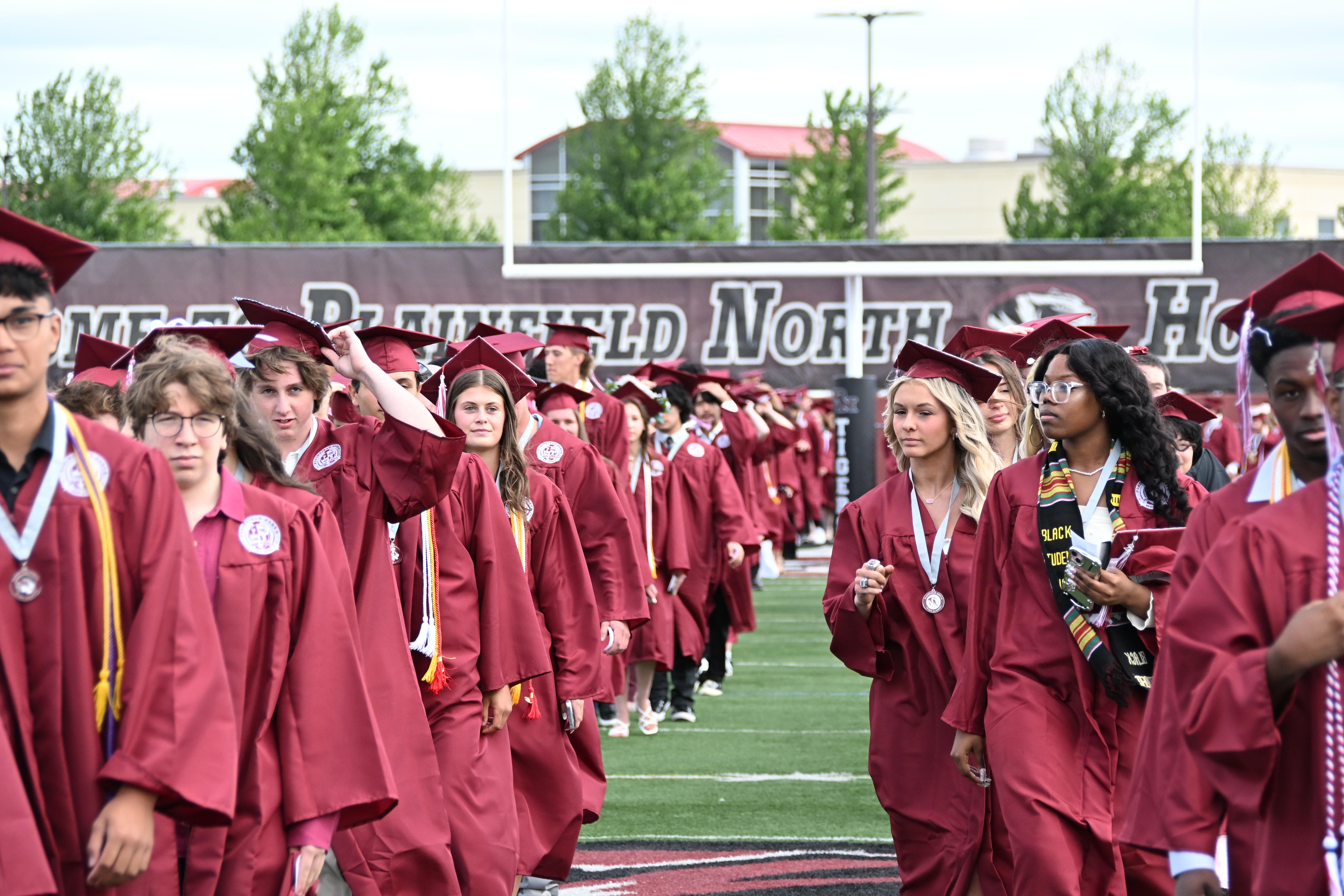 graduates in red gowns walk into stadium