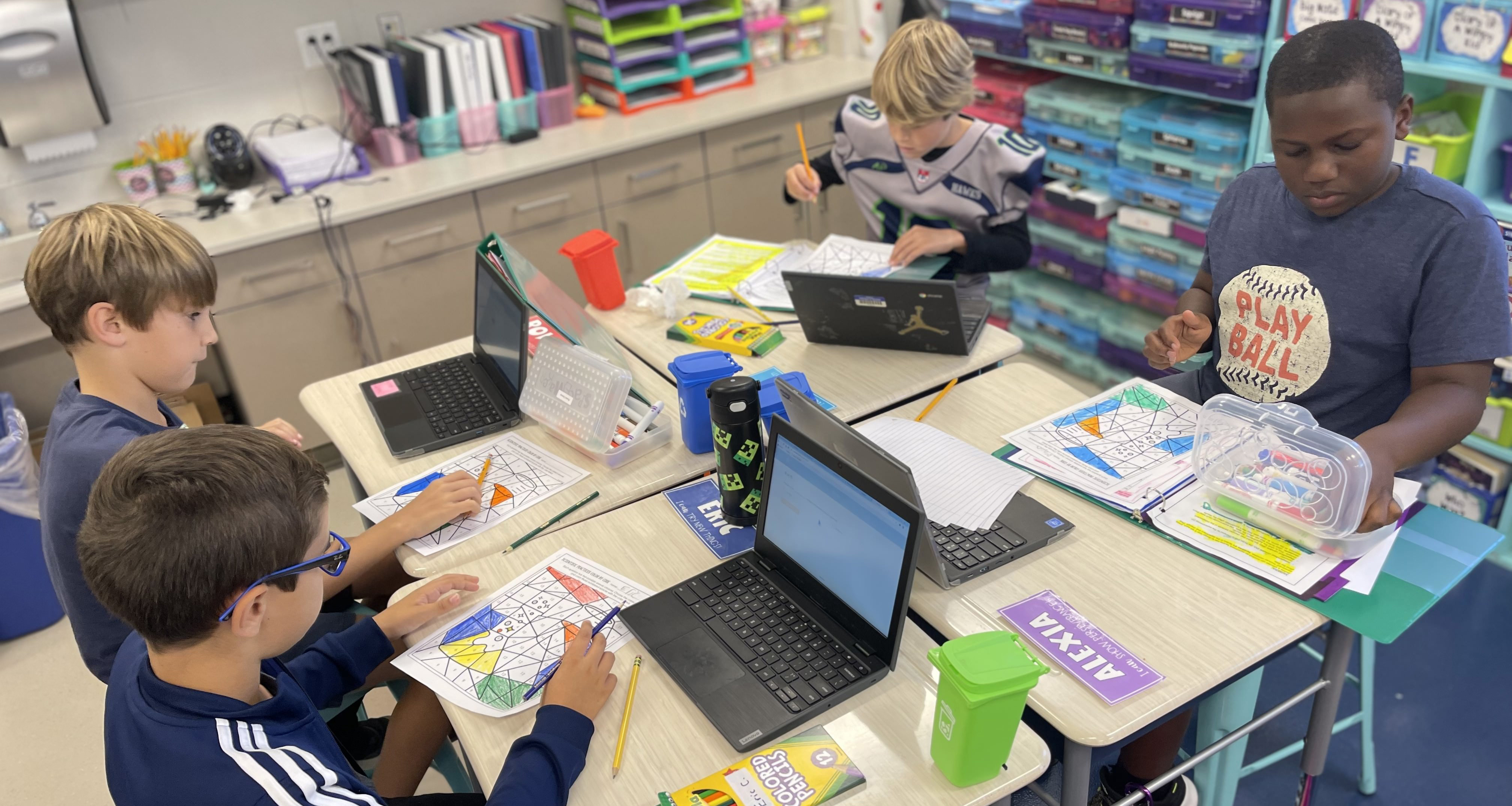 Four boys working on an assignment and using their laptops in class