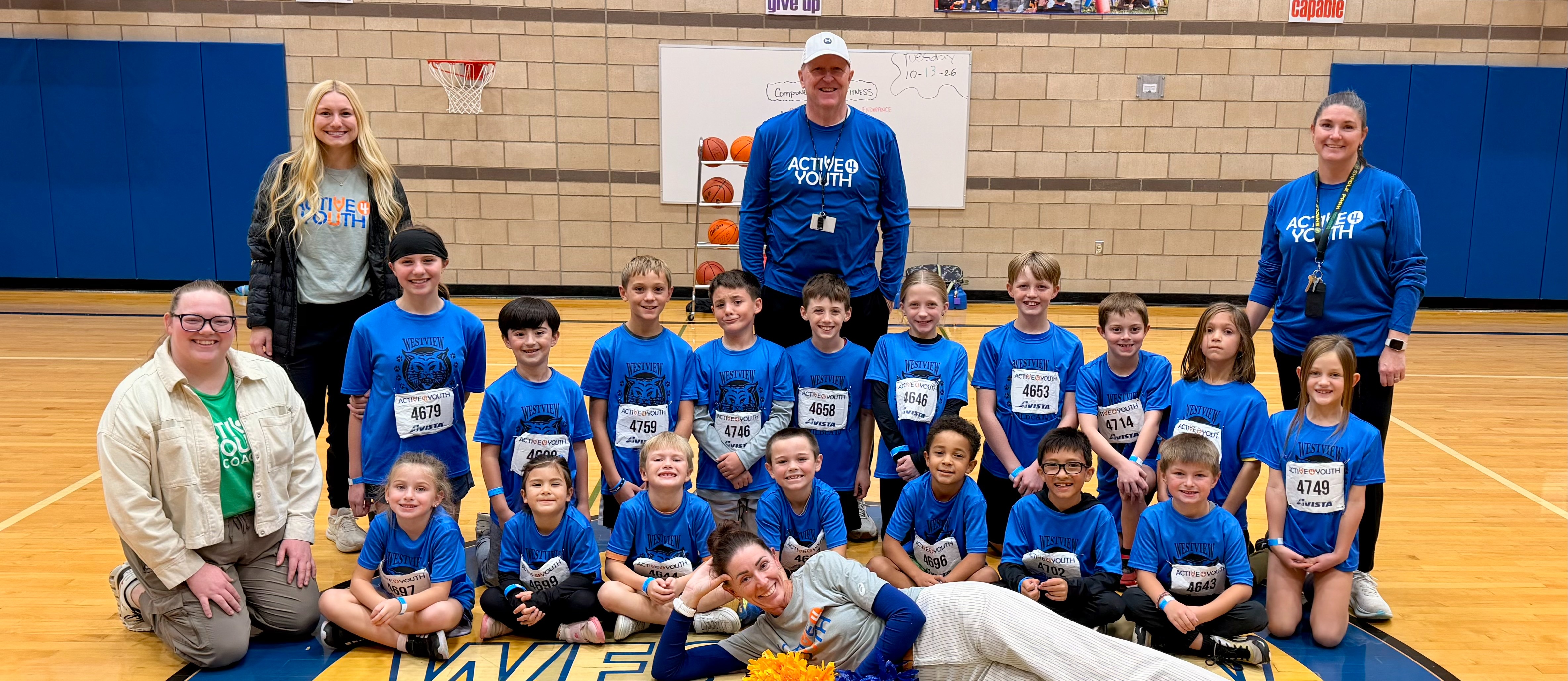 group of students wearing school jerseys posing in the gym with adults