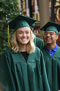 Two students smiling wearing green graduation gowns.