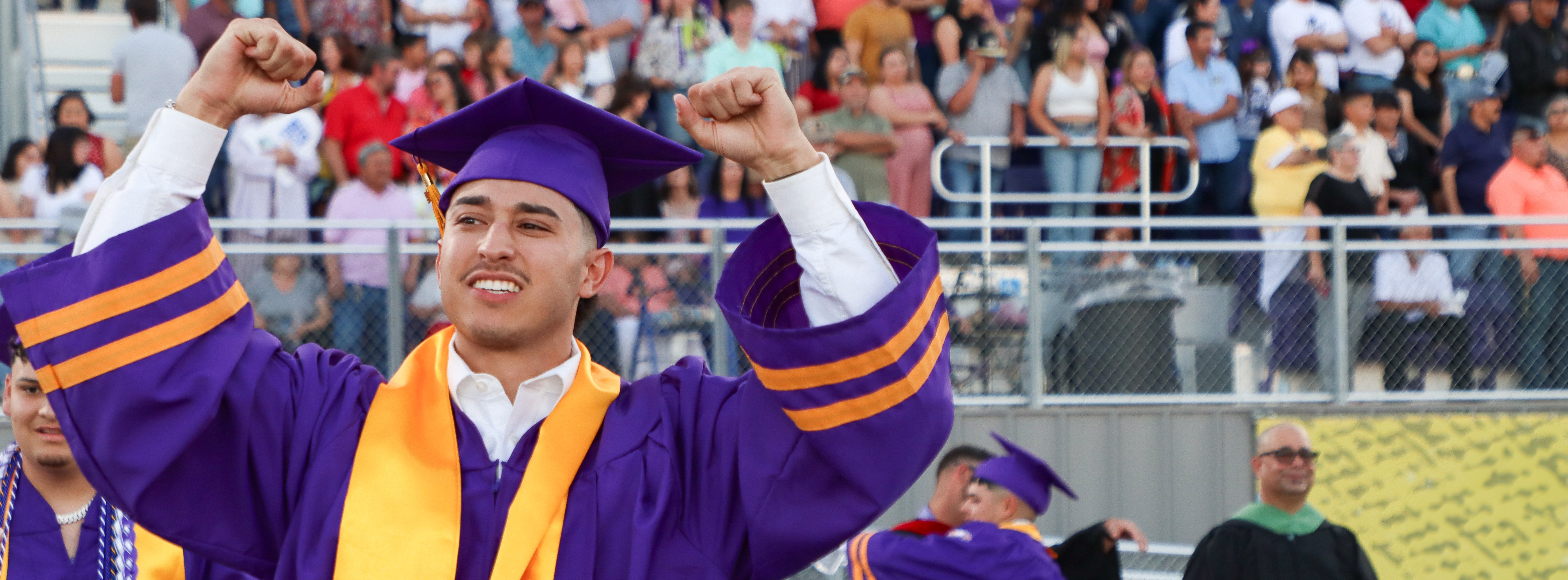 student holding arms in victory walking into graduation ceremony