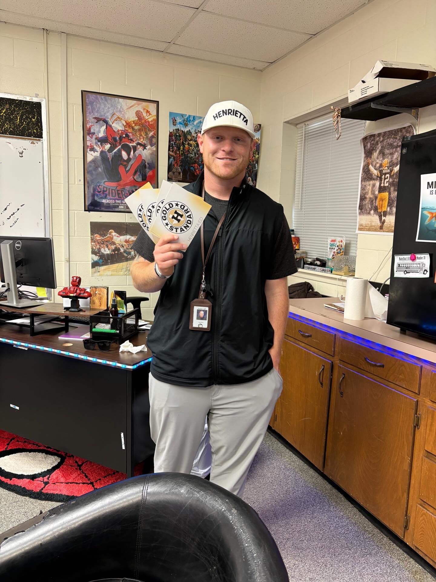 Man in black shirt, white cap, and gray pants holding tickets in an office with a desk.