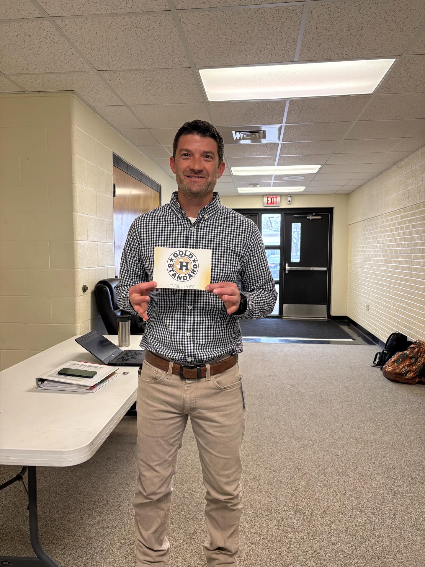 A man in a room holds up a yellow sign with the letters "H-S" on it.