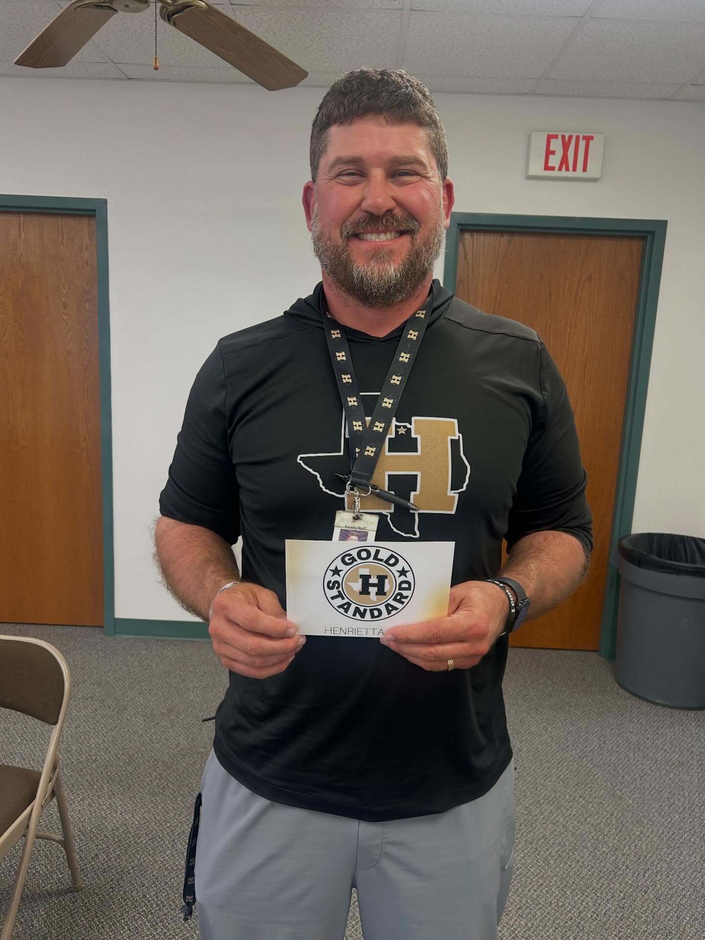 A man holds a card and ID badge in a room with white walls and wooden doors.
