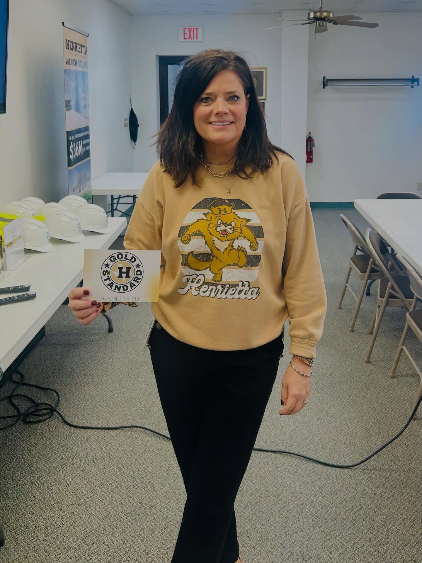 A woman holds a sign that reads "Gold Standard" while wearing a sweatshirt with a cartoon character.