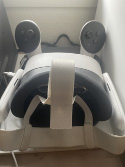 A white and gray virtual reality headset with controllers rests on a wooden surface with a white wall.