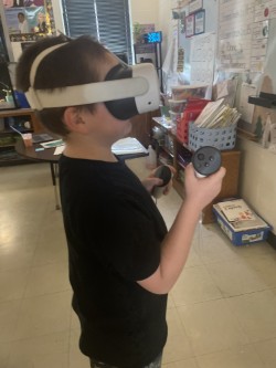 A child wears a virtual reality headset, holding controllers, and standing in a room with white tile floors.