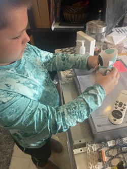 A child in a teal shirt examines a remote control. A white box sits on a countertop.