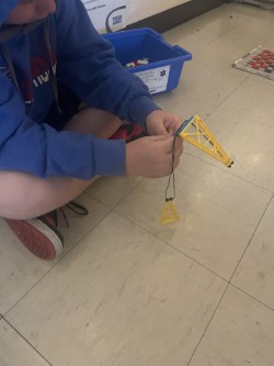 A person sits on a tiled floor, assembling a yellow crane model. A blue bin is behind them.