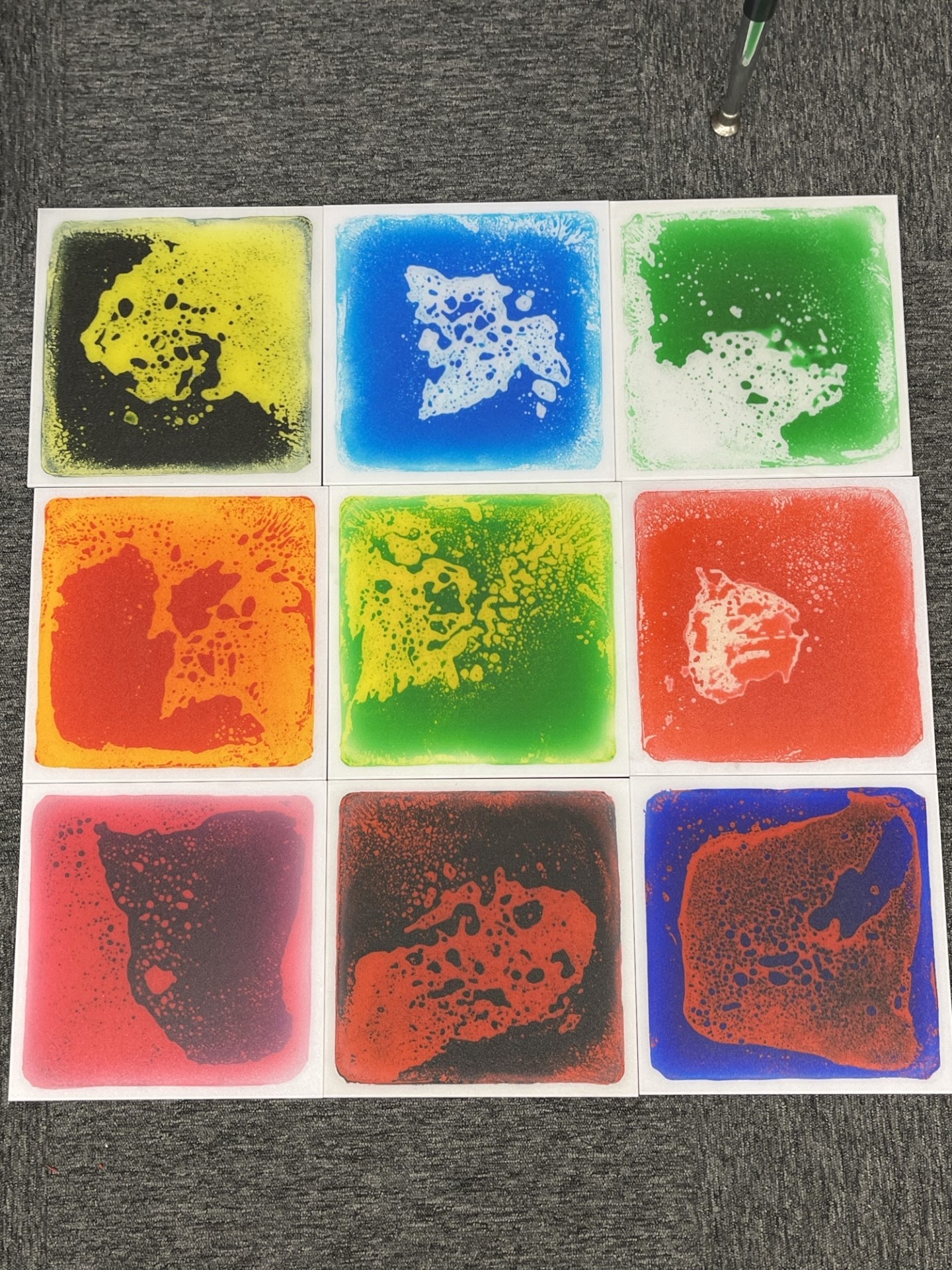 A grid of nine colorful squares with various abstract shapes and patterns. The colors range from dark to light and include red, yellow, blue, and green.