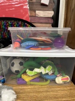 A plastic container filled with various toys and a soccer ball sits on a wooden surface.