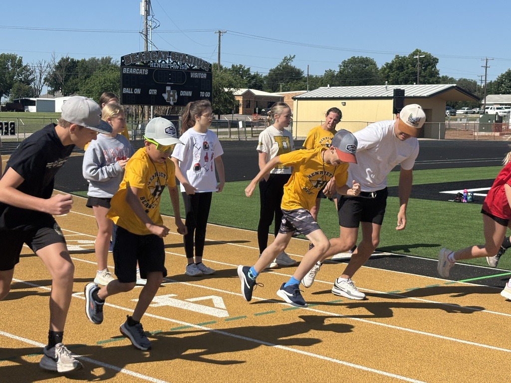 Group of people, some wearing caps and sneakers, running on a track with white lines.