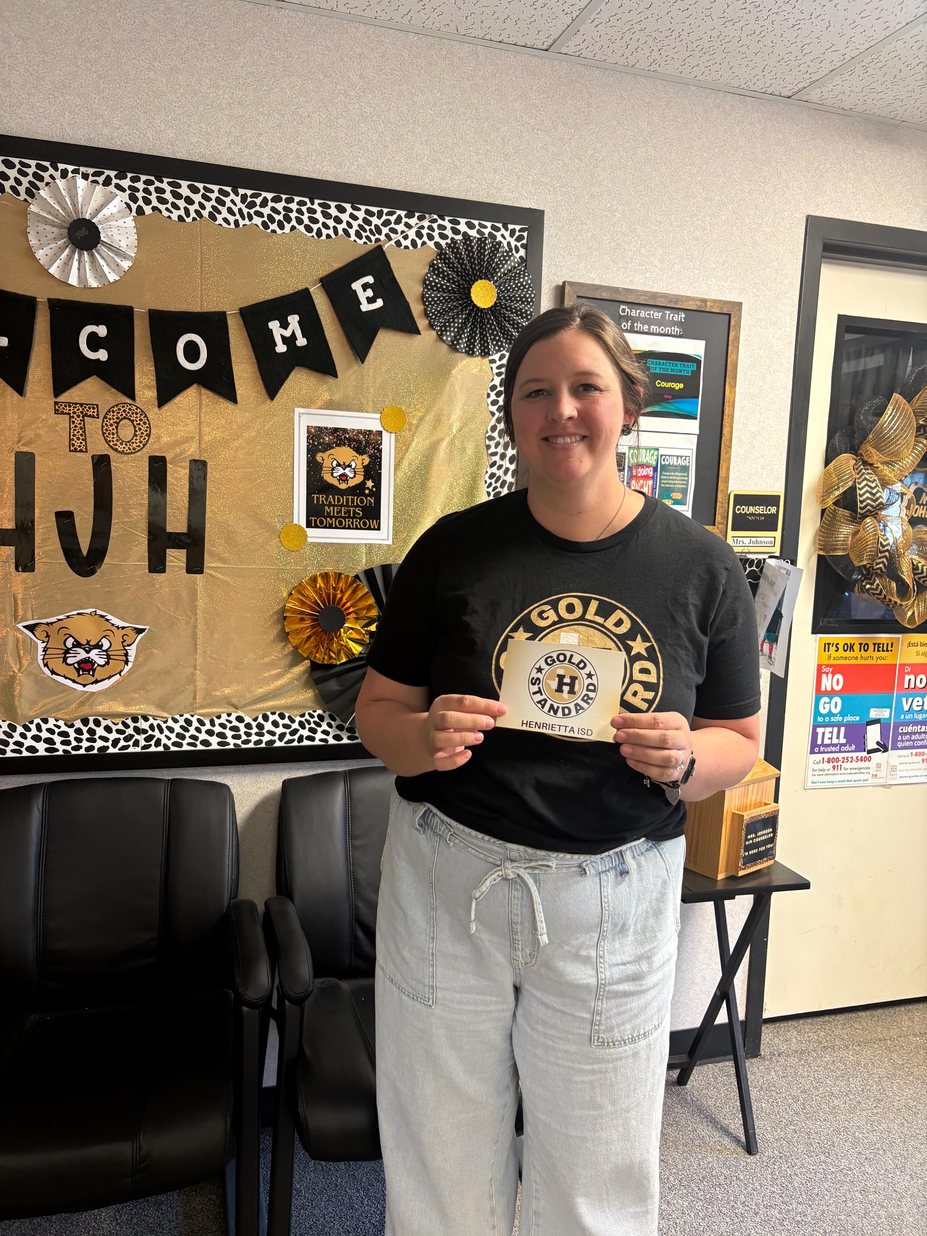 Person holding an award in front of a bulletin board that reads "Welcome to HJH".