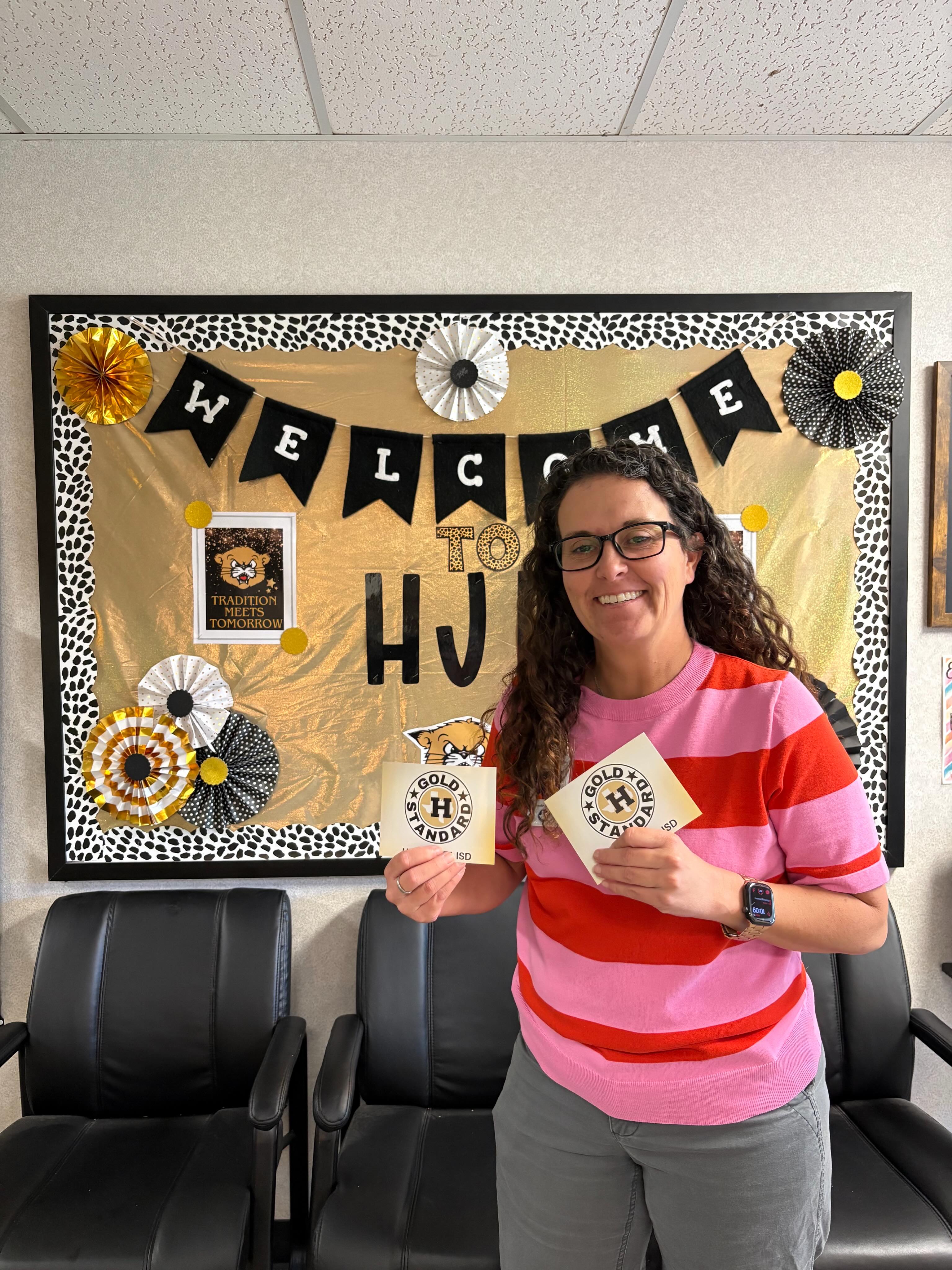 Woman with glasses holds cards in front of a welcome bulletin board.