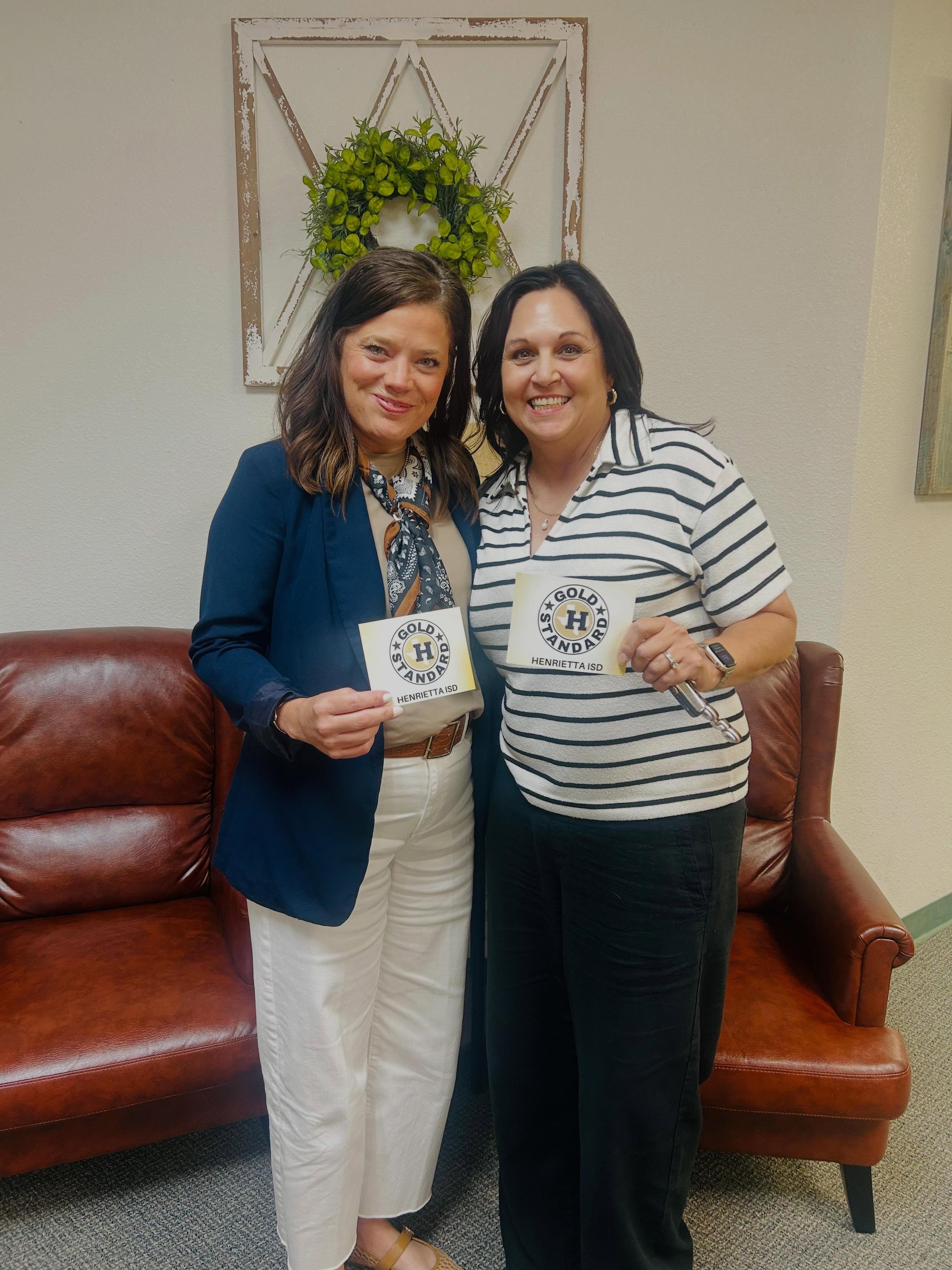 Two women in a room with a couch, one holding a mug with the words "MADE 11".