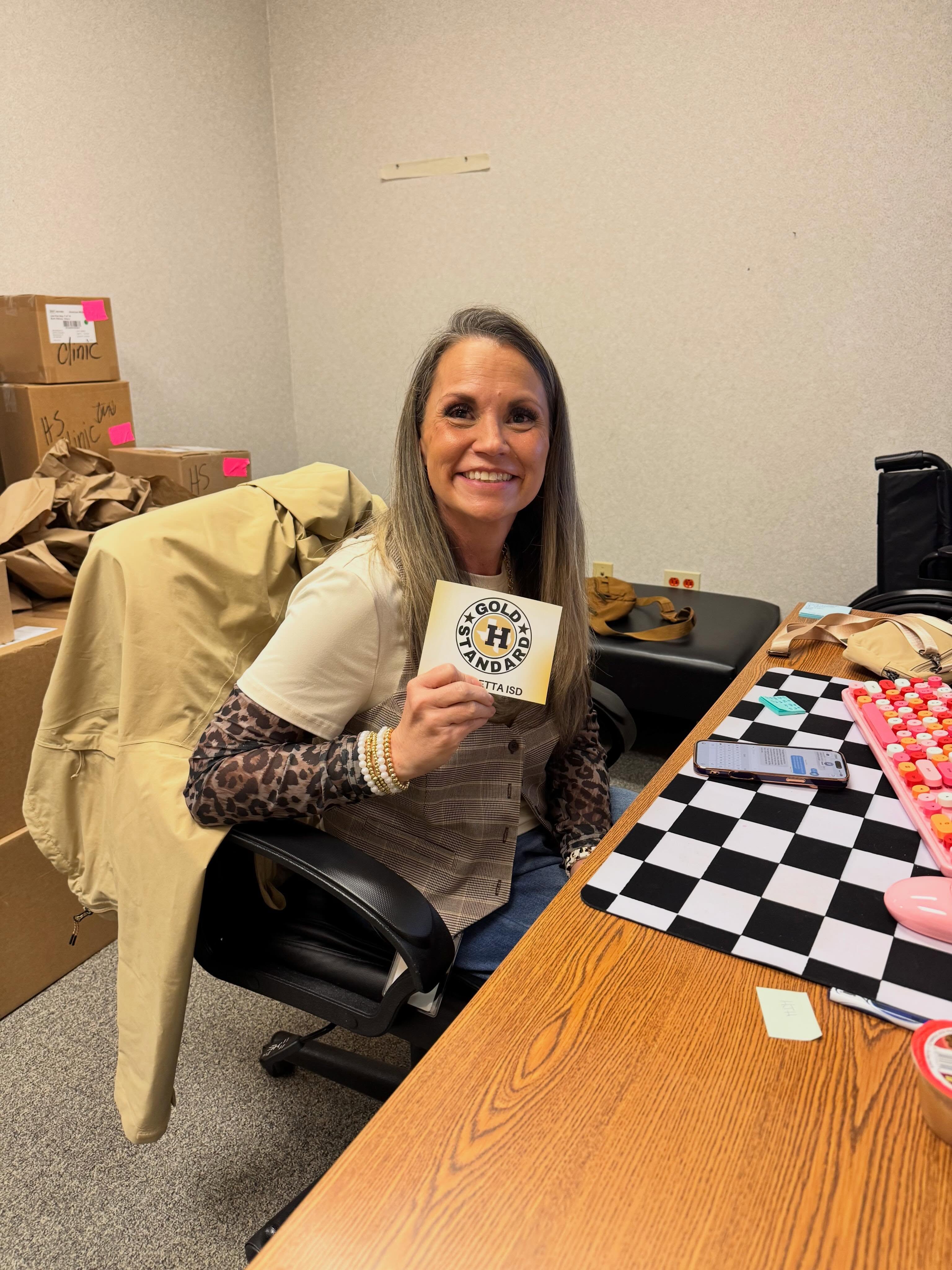 Woman sitting in a chair, holding a card with a logo, in a room with boxes and a table.