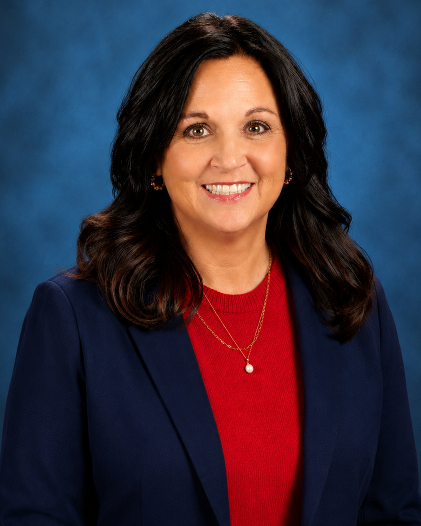 Woman with dark hair smiles at camera. She wears a blue blazer and red top. Background is blue.
