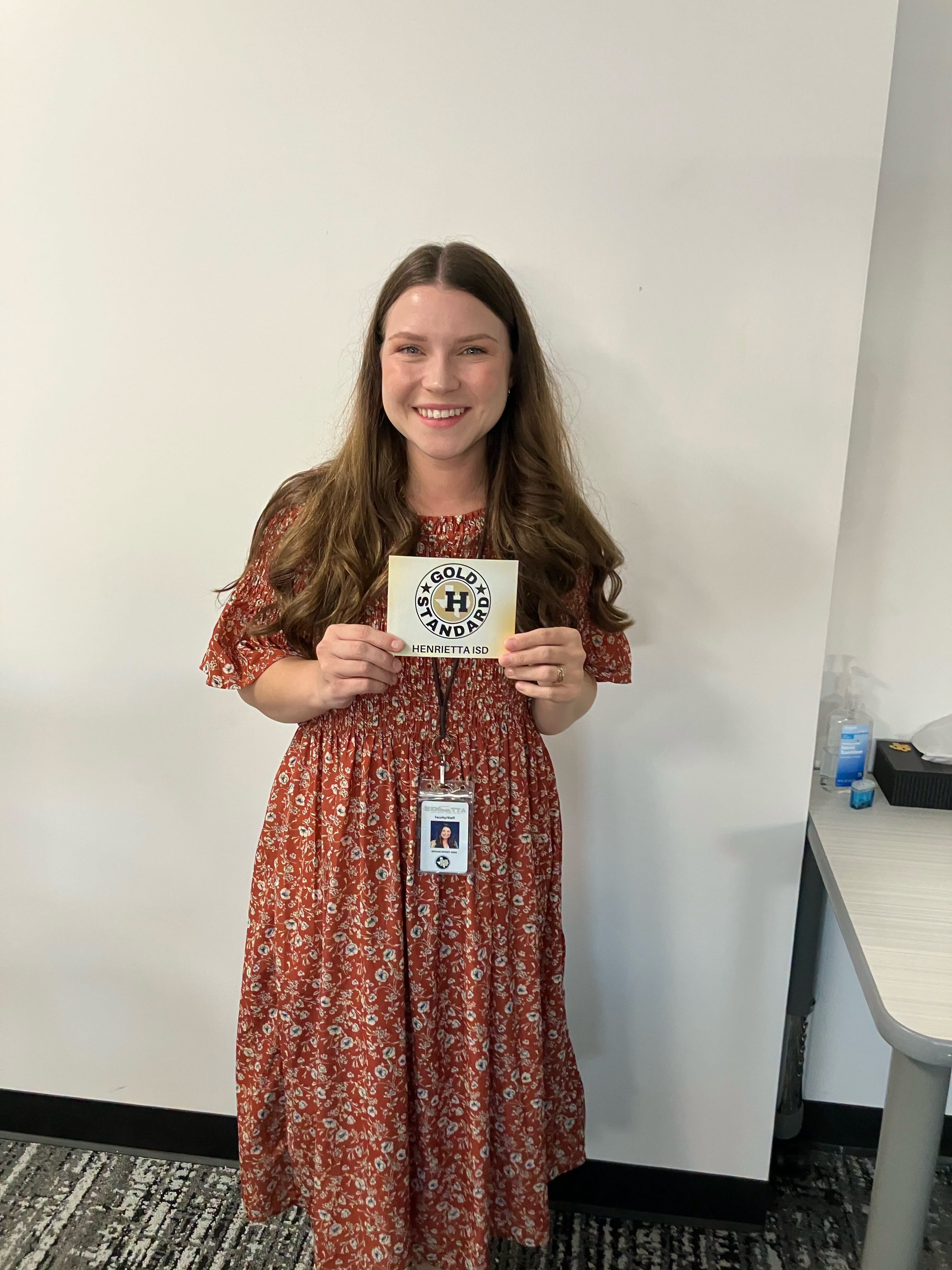 A woman in a floral dress holds a card with "Holistic" printed on it in an indoor office.