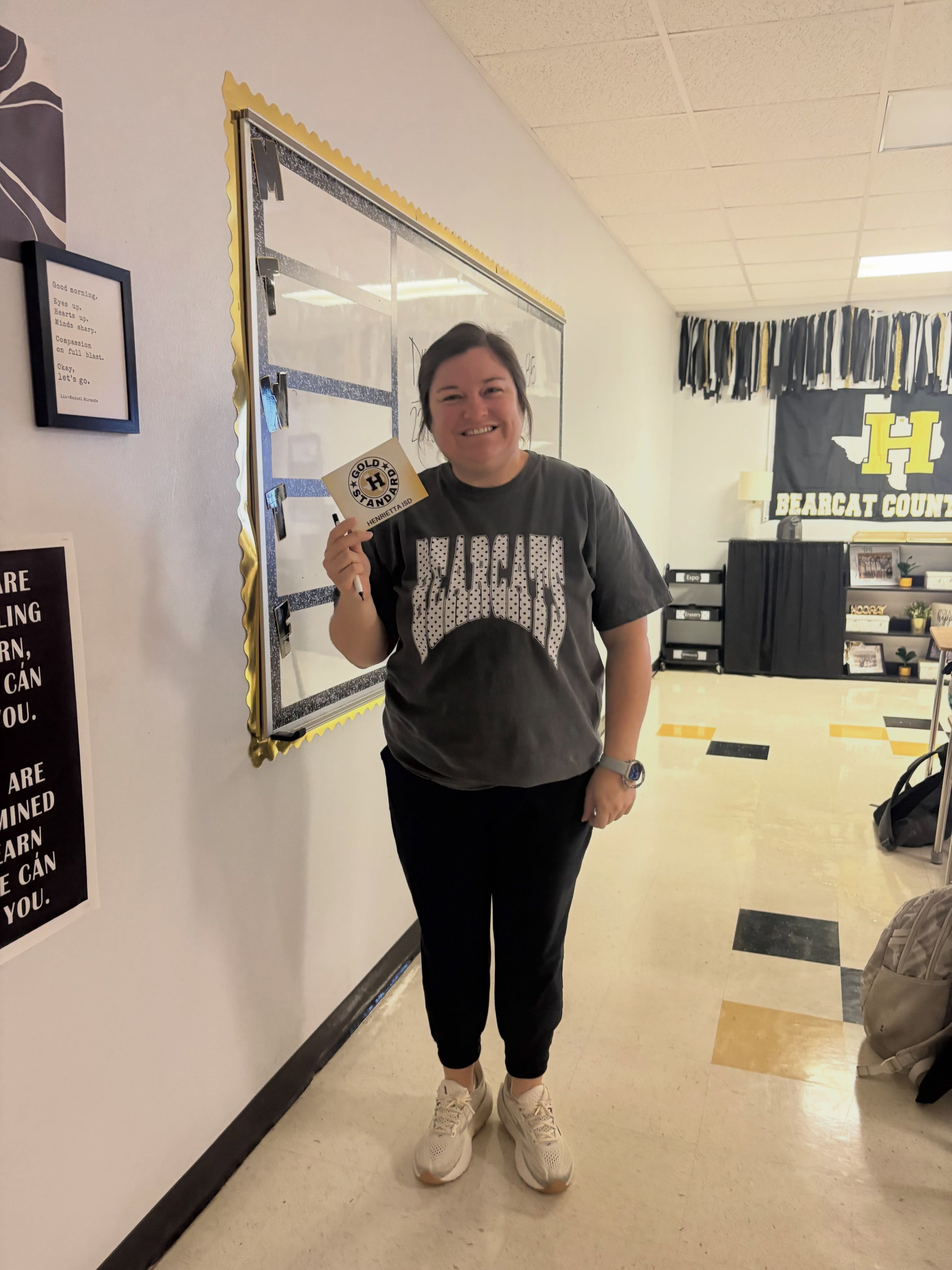 Person in black pants and gray T-shirt stands in a hallway with a motivational poster.