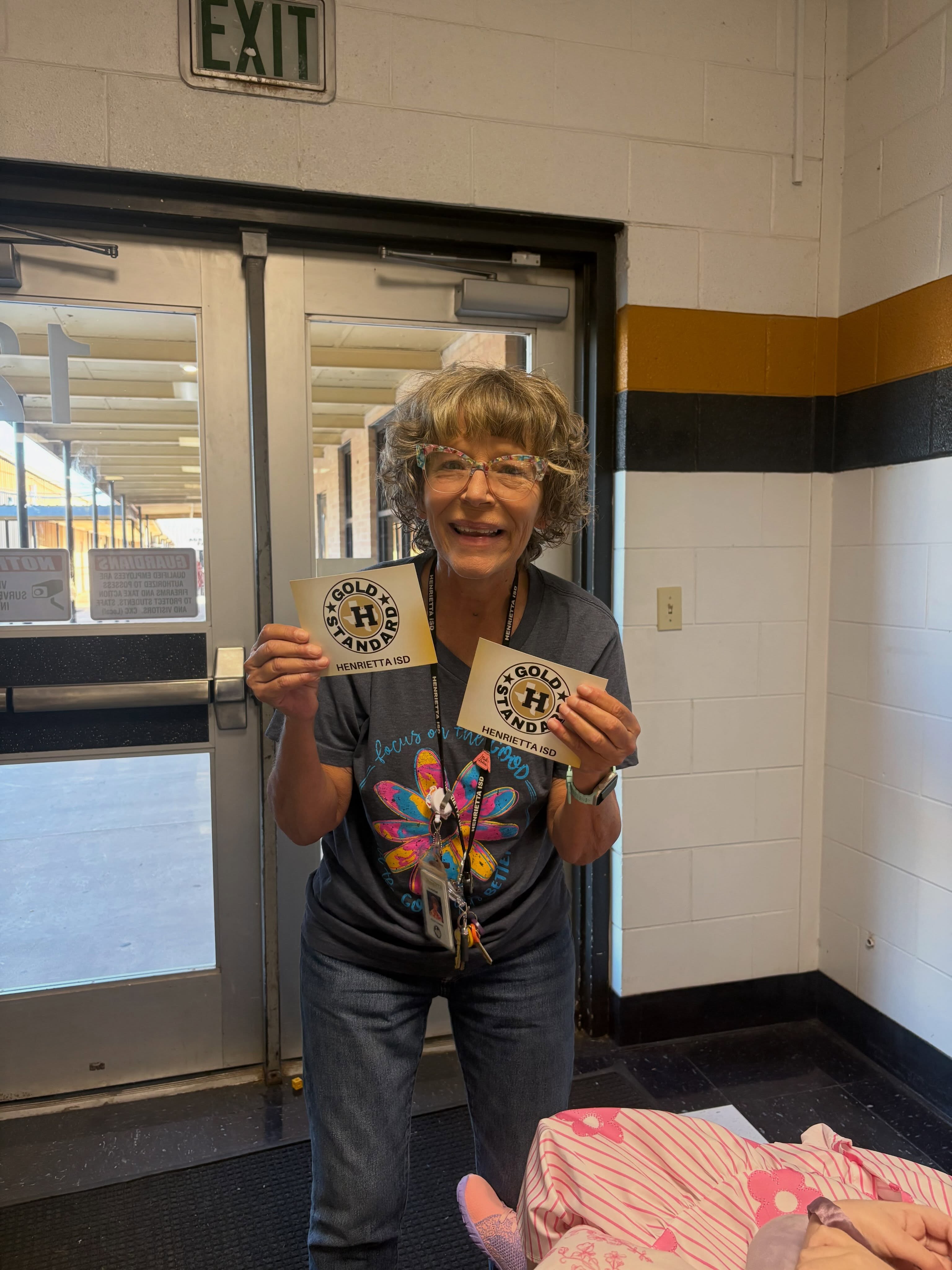 Woman in jeans holding two circular items in front of a building door with an exit sign above.