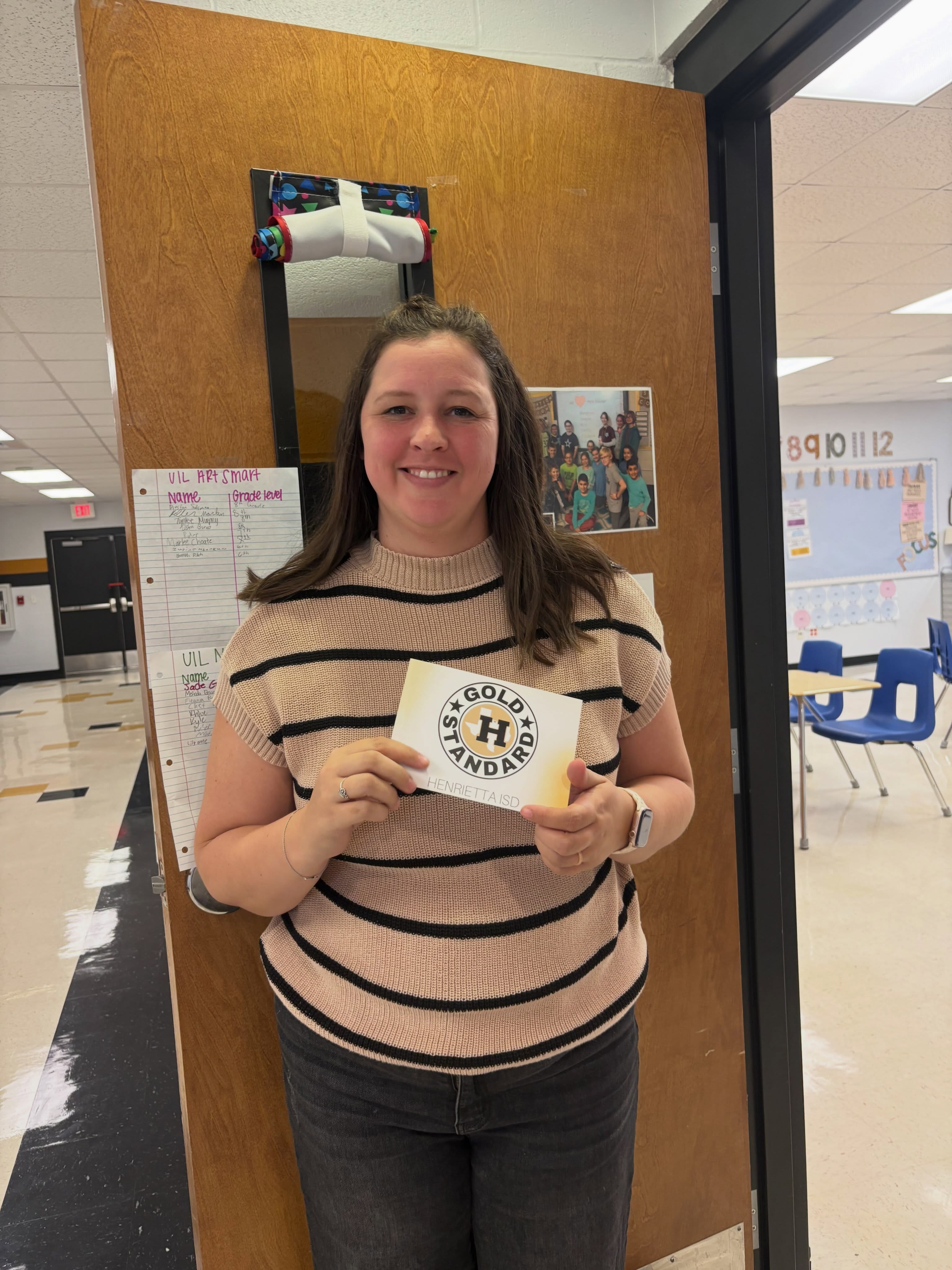 A woman stands by a door, holding a card with "Golden Hands" written on it. She wears a striped shirt.