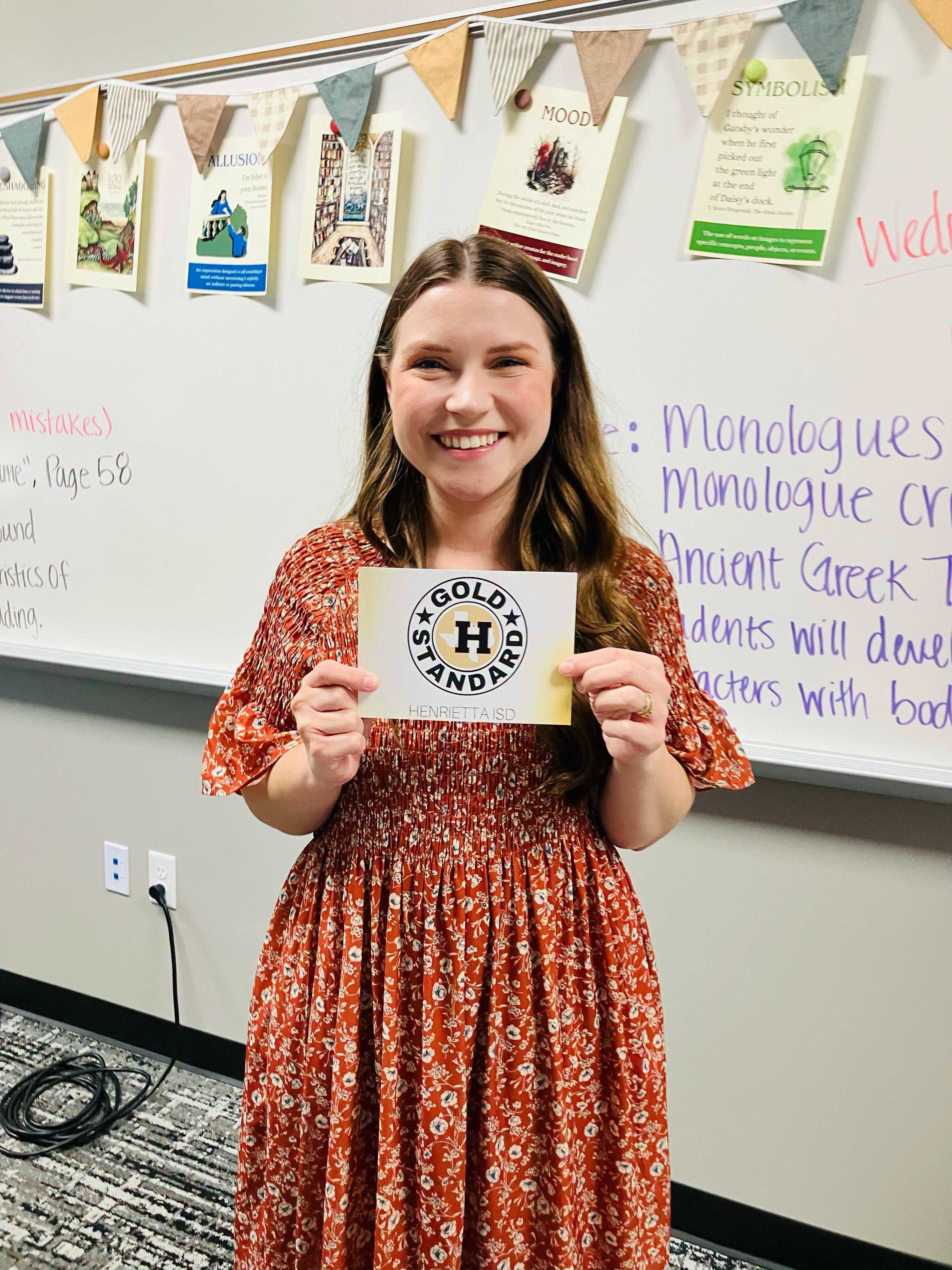 A woman holds a certificate in a classroom with a white board and decorations.
