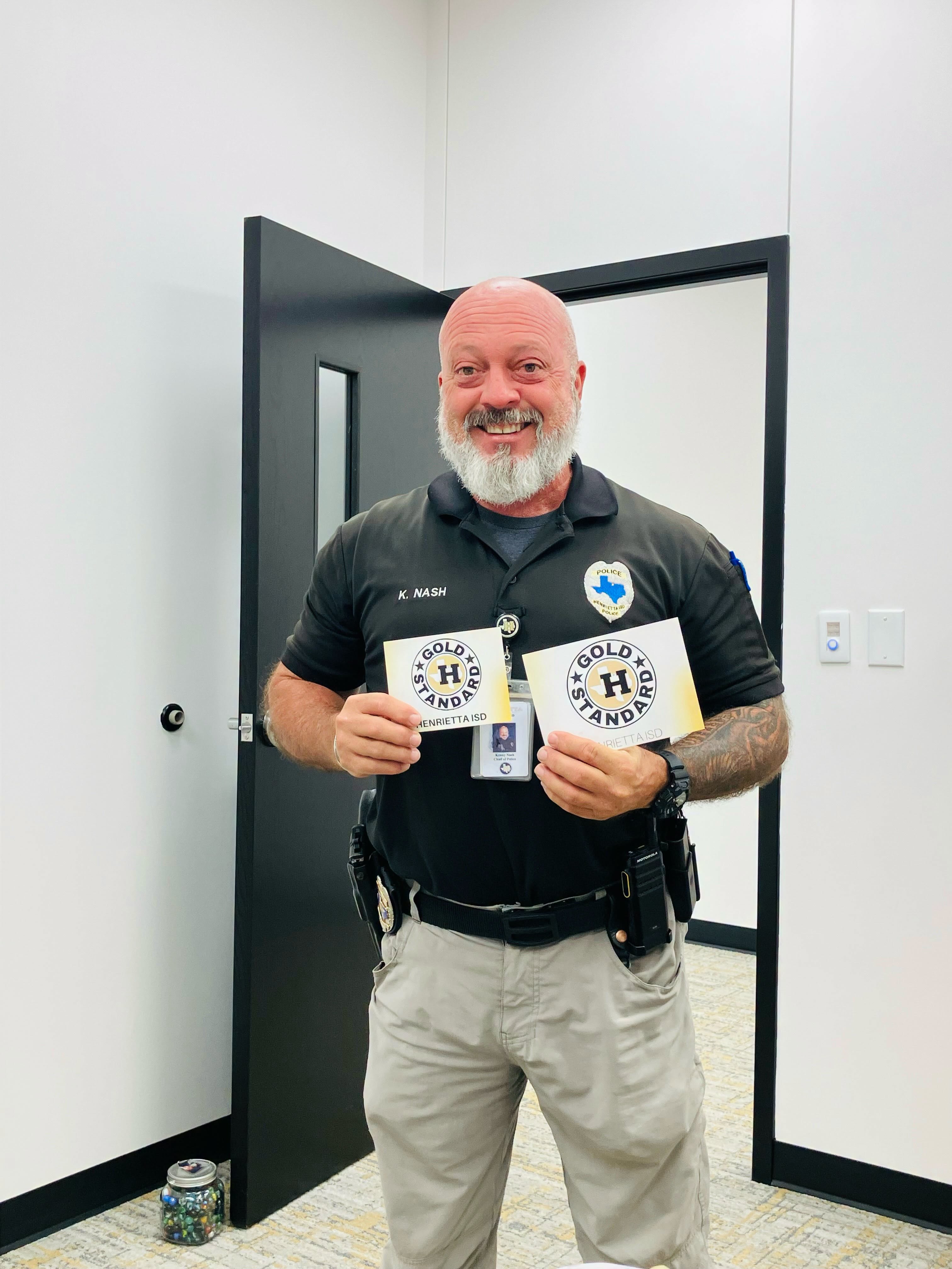 A man in a police uniform holds up two yellow cards in a room with white walls and black doors.