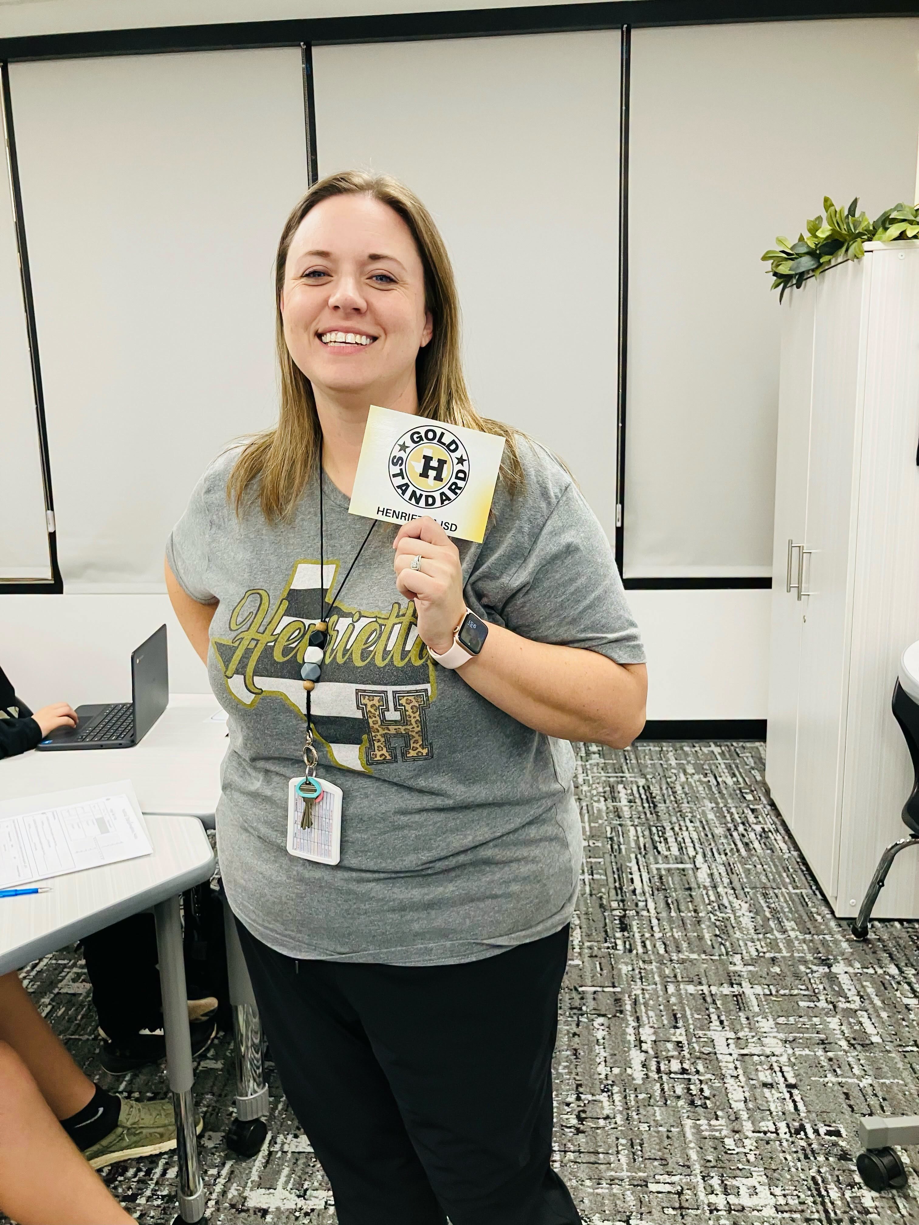 Woman in gray shirt holding up a yellow card with black text standing in a classroom.