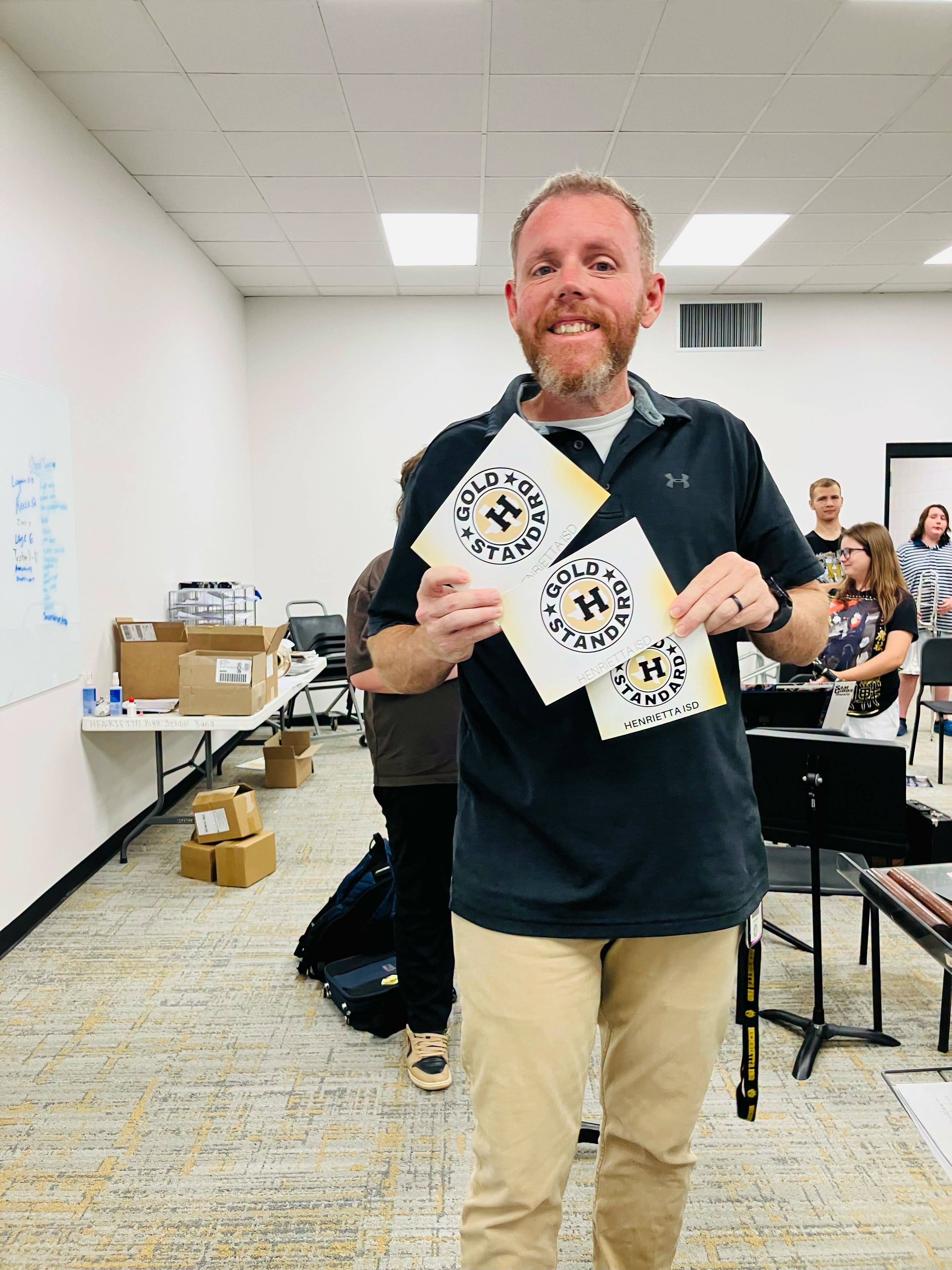 Man holding up two white cards with yellow writing in a room with tables and chairs.