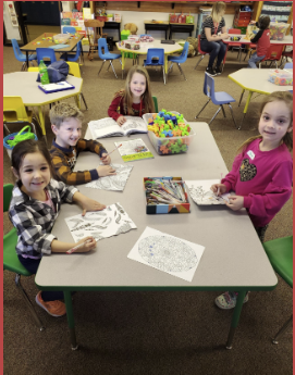 several preschool aged kids sitting at a desk in a classroom smiling 