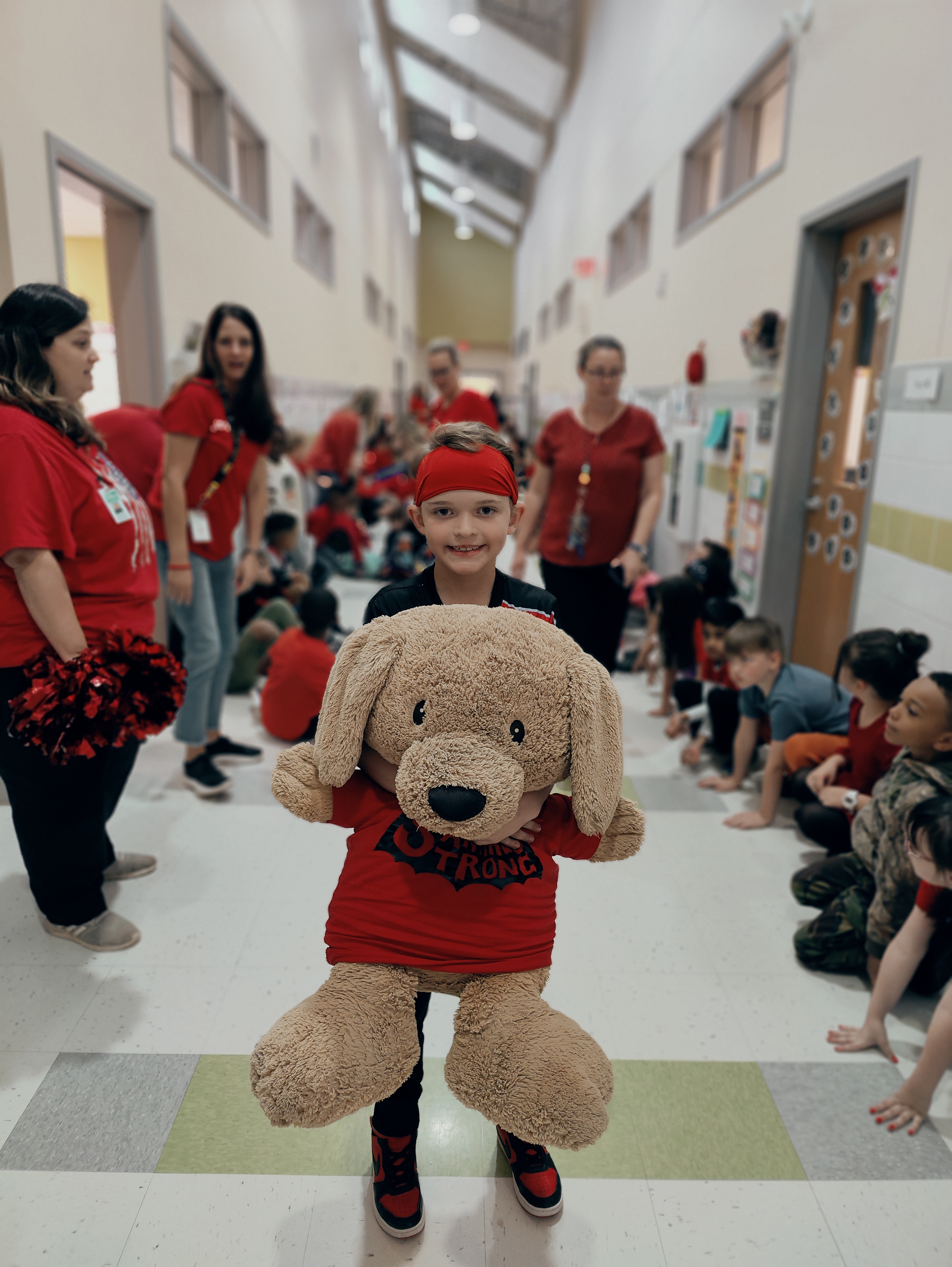 students smiling wearing red hold a bear