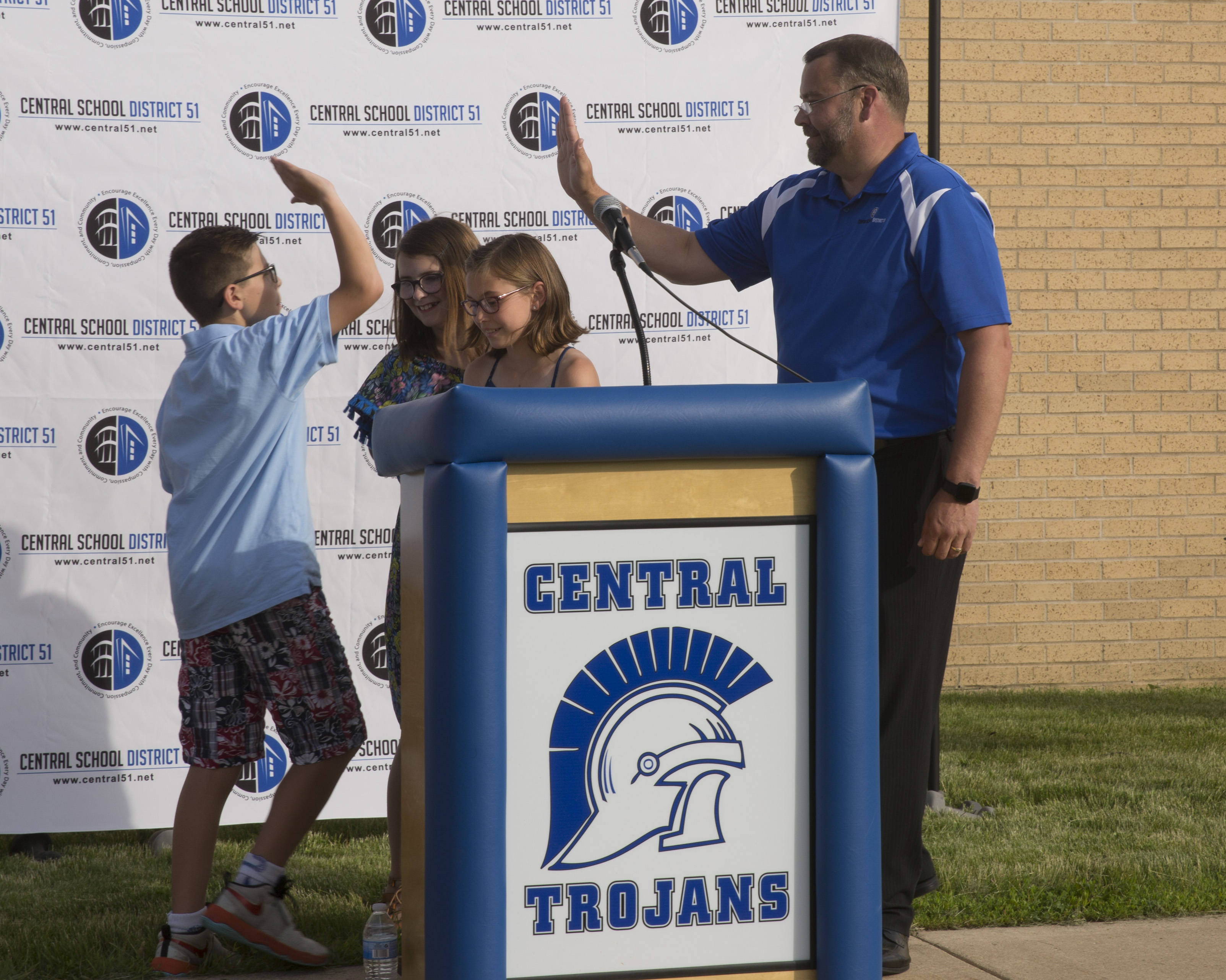 The same three little kids going off the stage and one of the high fiving the superintendent.