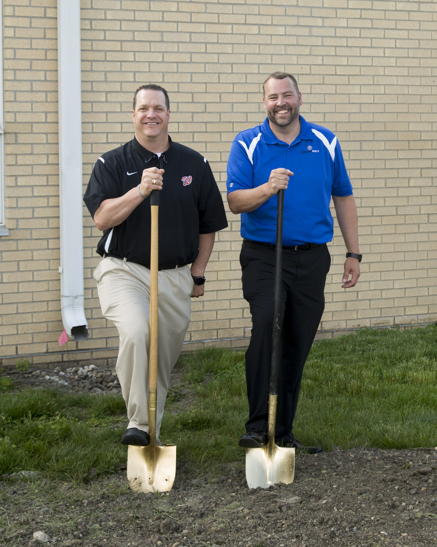 The superintendent and the principal smiling up at the camera and holding up a shovel each.