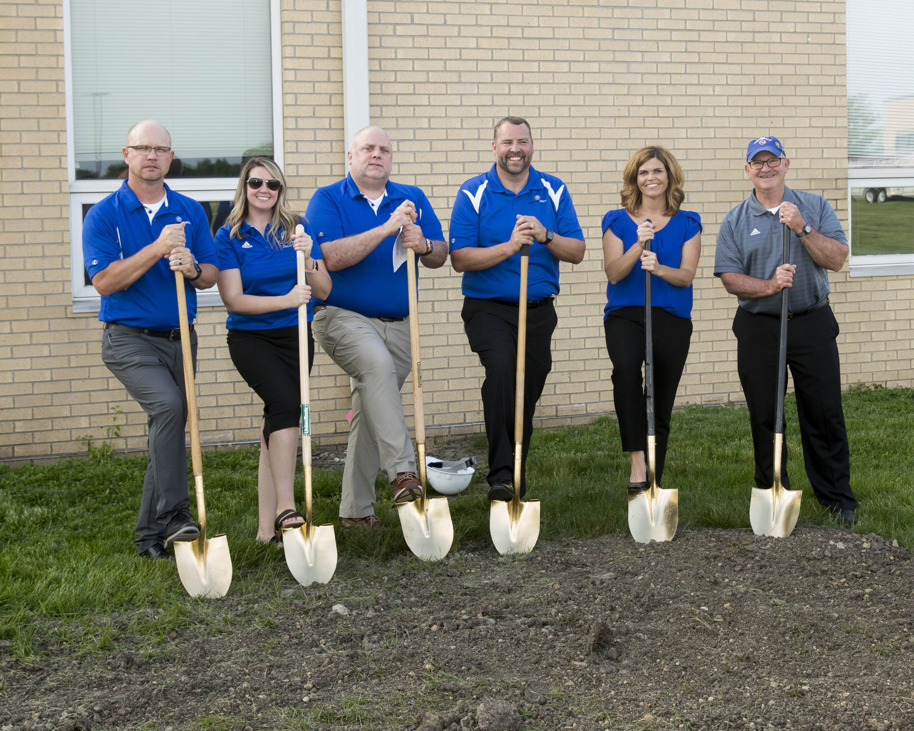 The teachers all wearing a polo blue shirt and posing with a shovel in their hands.